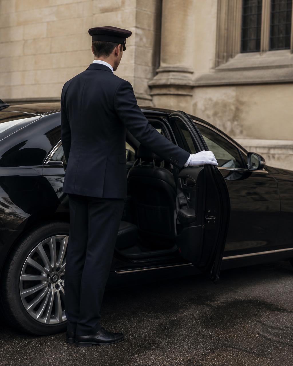 Chauffeur in a tailored suit opening the rear door of a black luxury saloon in Oxford